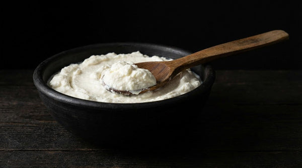 Bol cu urdă cremoasă proaspătă de vacă tip Ricotta — textură fină untoasă, servită cu lingură de lemn rustic